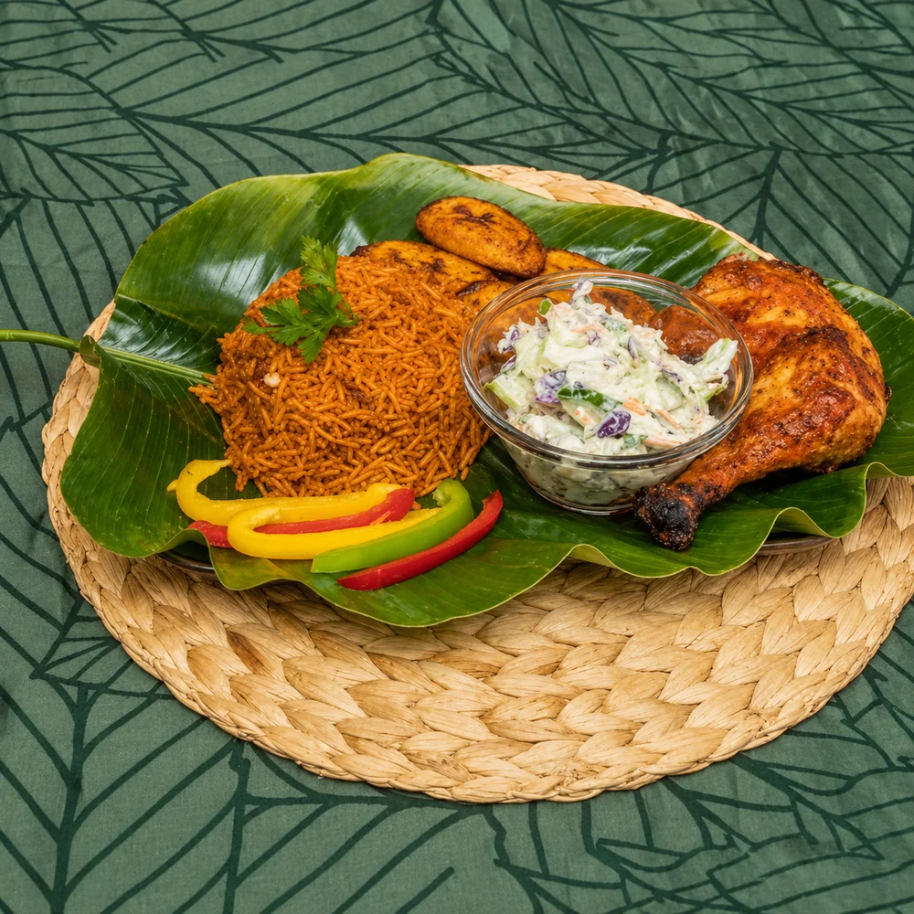 Jollof rice with grilled chicken, fried plantain and coleslaw, served on a banana leaf